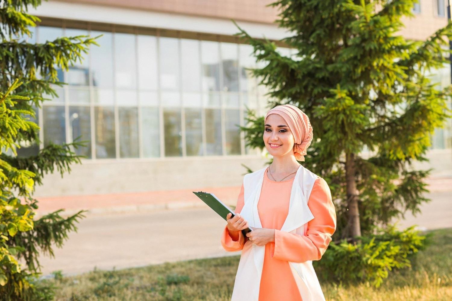 Young female BTEC graduate holding a clipboard outside a university building